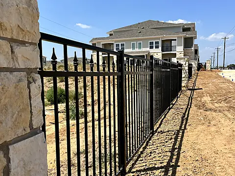 Spear-top ornamental steel fence running from a stone column at a new apartment community