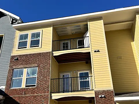 Black steel balcony railings on a three-story apartment building with yellow siding