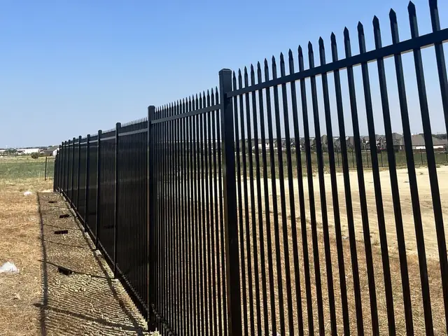 Spear-top steel security picket, points above the top rail, along a graded site perimeter