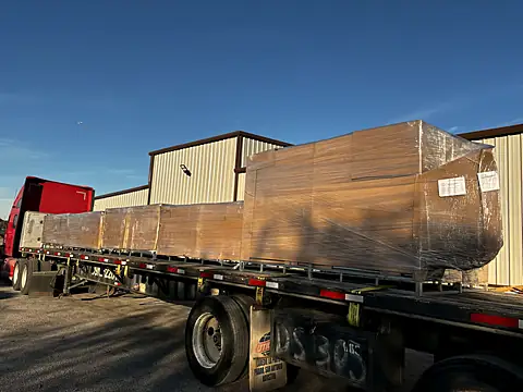 Flatbed trailer loaded with crated, shrink-wrapped and labeled fence panels outside a warehouse